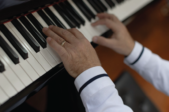 Close-up of a composer’s hands playing piano keys, wearing a white shirt with dark cuffs and a wedding ring, conveying a professional music setting—ideal for those looking to purchase music arrangements.